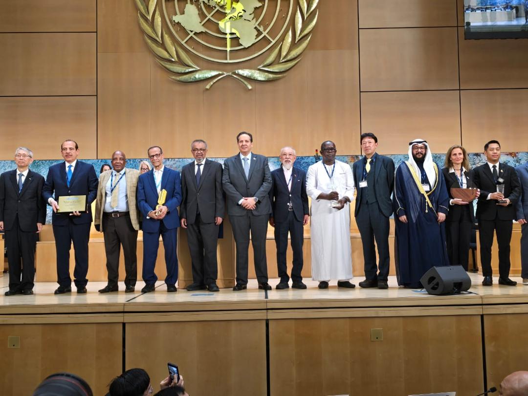 Lauréats du Prix Sasakawa pour la Santé devant l'emblème de l'OMS à Genève